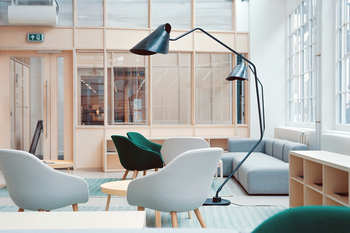 Bright and airy interior photograph of a styled living corner with a comfortable sofa, wooden side tables, statement decorative lighting, greenery and framed texture details, natural daylight, calm color palette, no people
